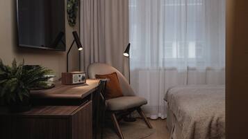Un dormitorio moderno con una cama, un escritorio con una computadora, una silla y un televisor en la pared.