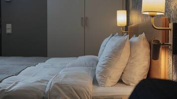 Una cama bien hecha con sábanas y almohadas blancas, una lámpara de pared y un cabecero de madera.