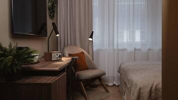 Un dormitorio con cama, escritorio con radio, silla, televisor y ventana con cortinas.