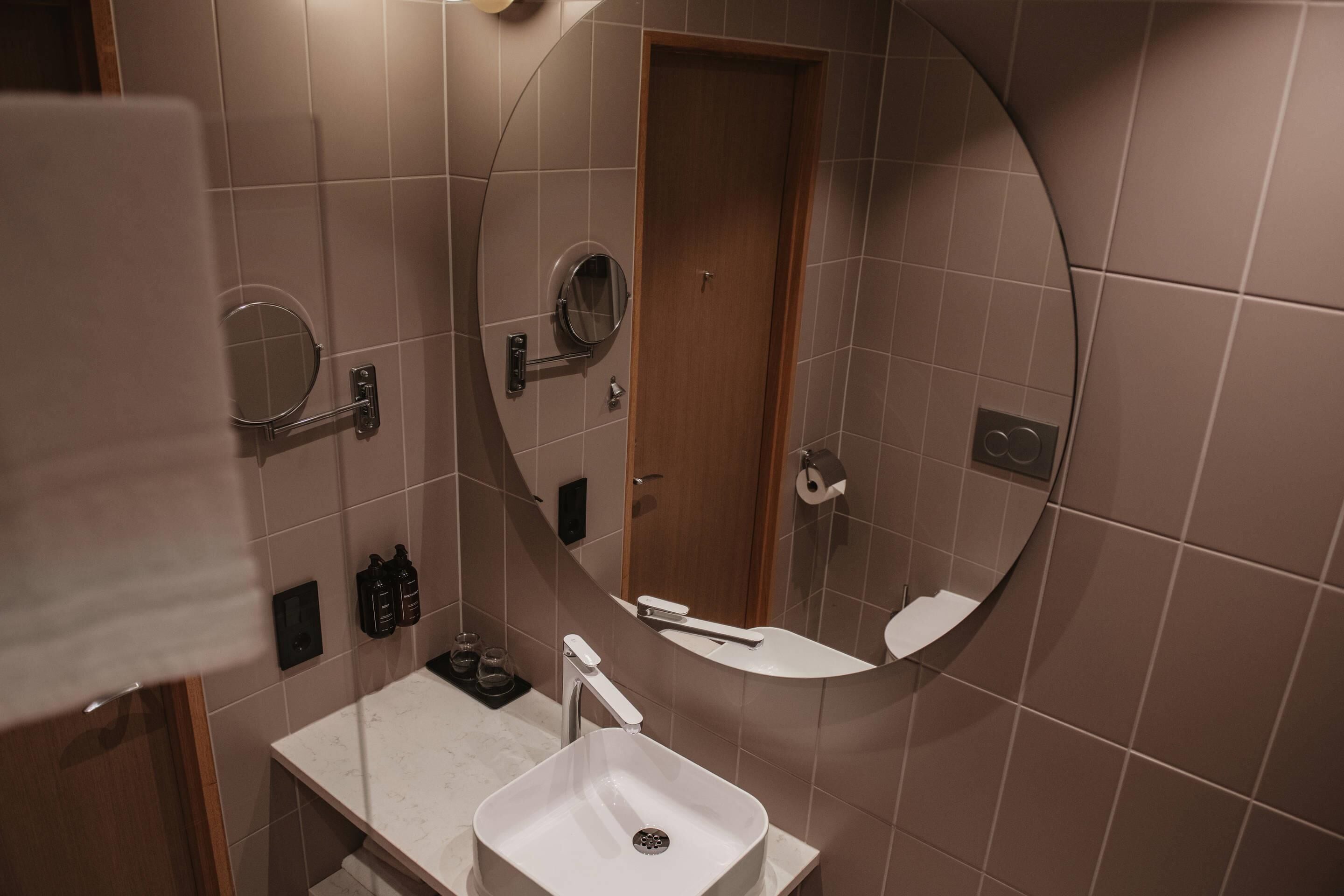 A bathroom with a white sink, a round mirror, and a wooden door.