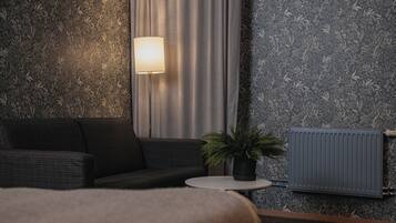 Ein modernes Zimmer mit einer dunklen Couch, einem runden Tisch mit Topfpflanze, einer Wandlampe und einer Heizung.