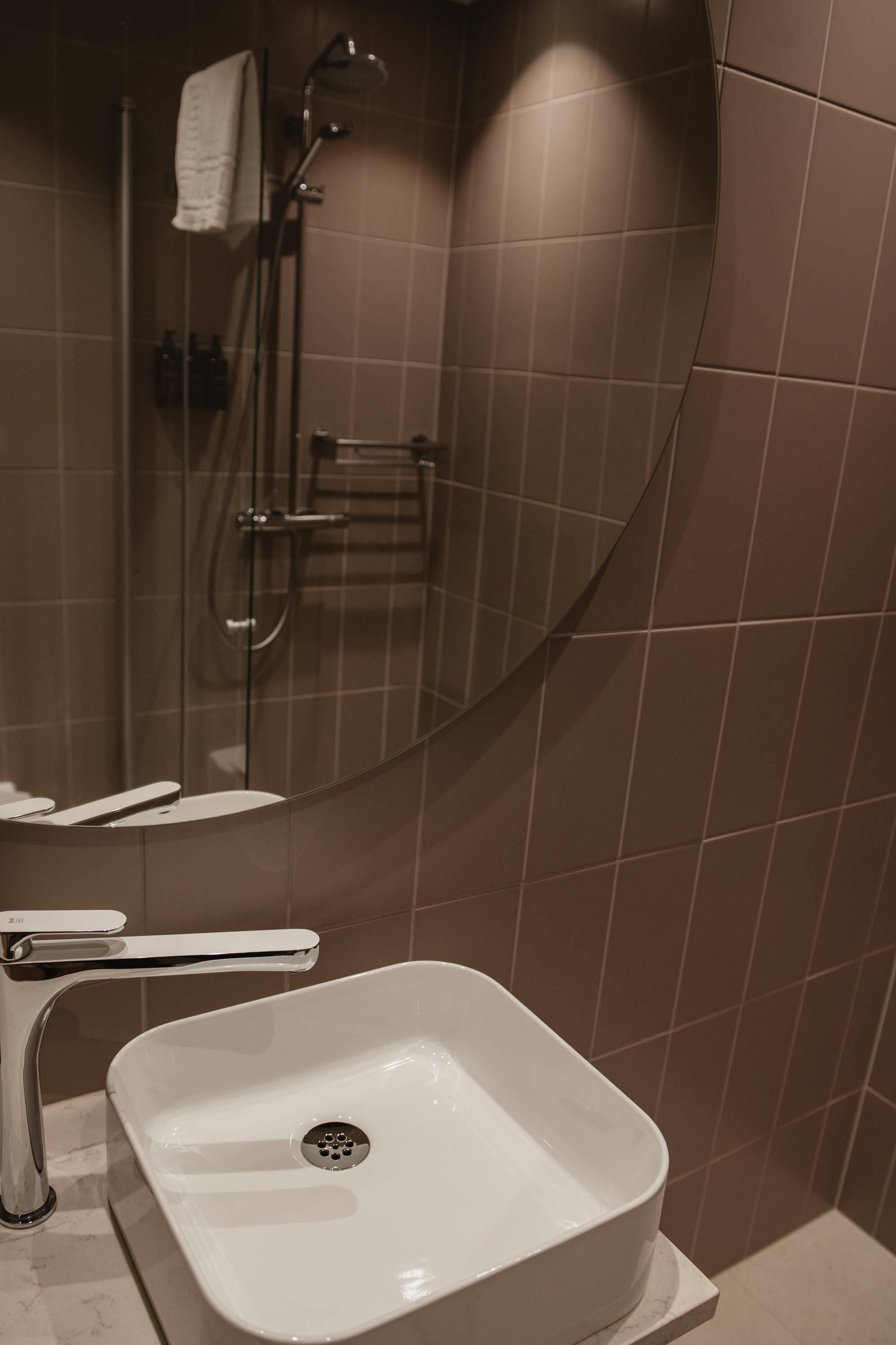 Ein Badezimmer mit einem weißen Waschbecken, einer Duschkabine aus Glas und einem Handtuch an einem Haken.