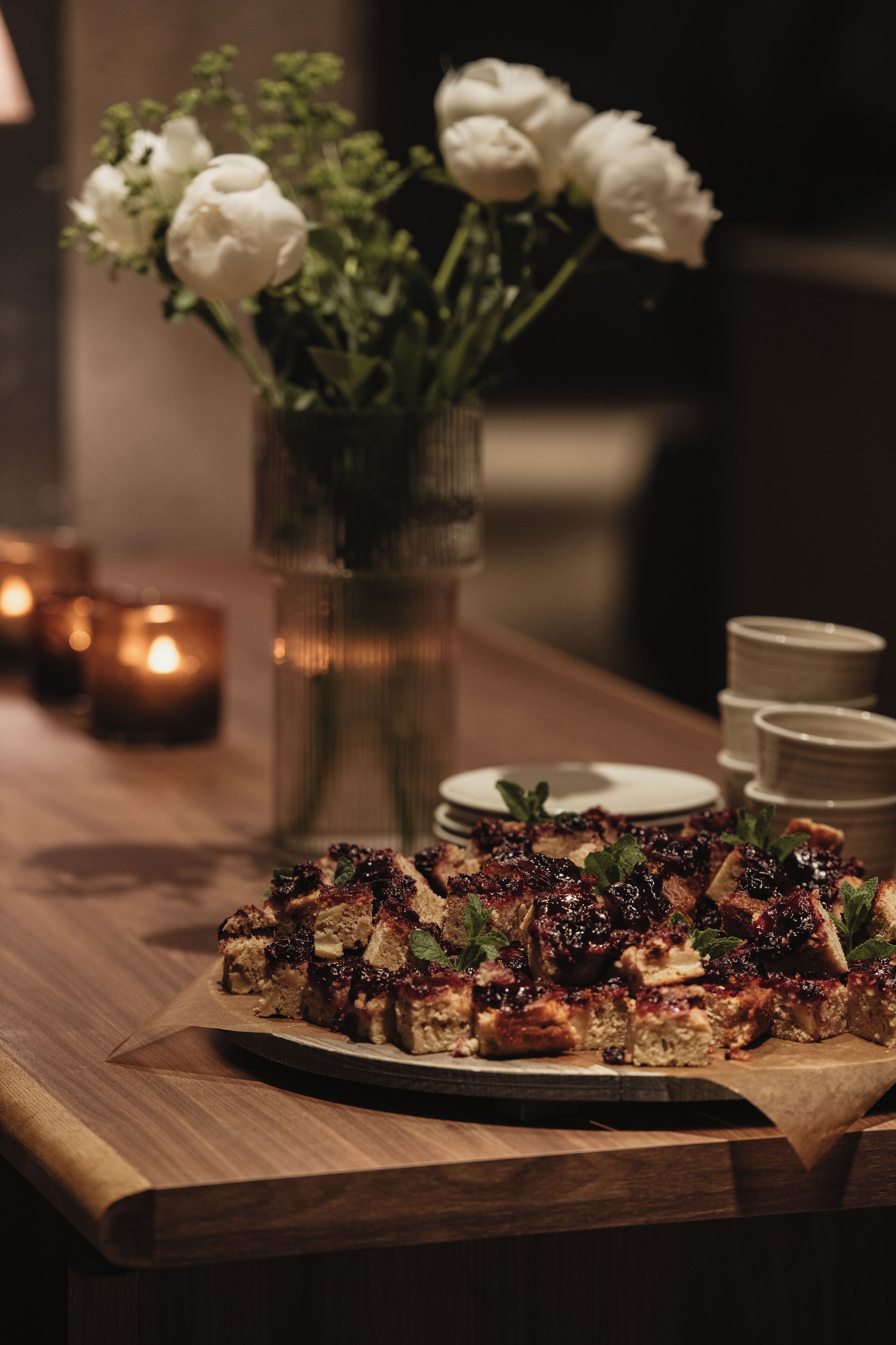 A wooden table with a pizza, candles, and a vase of flowers.