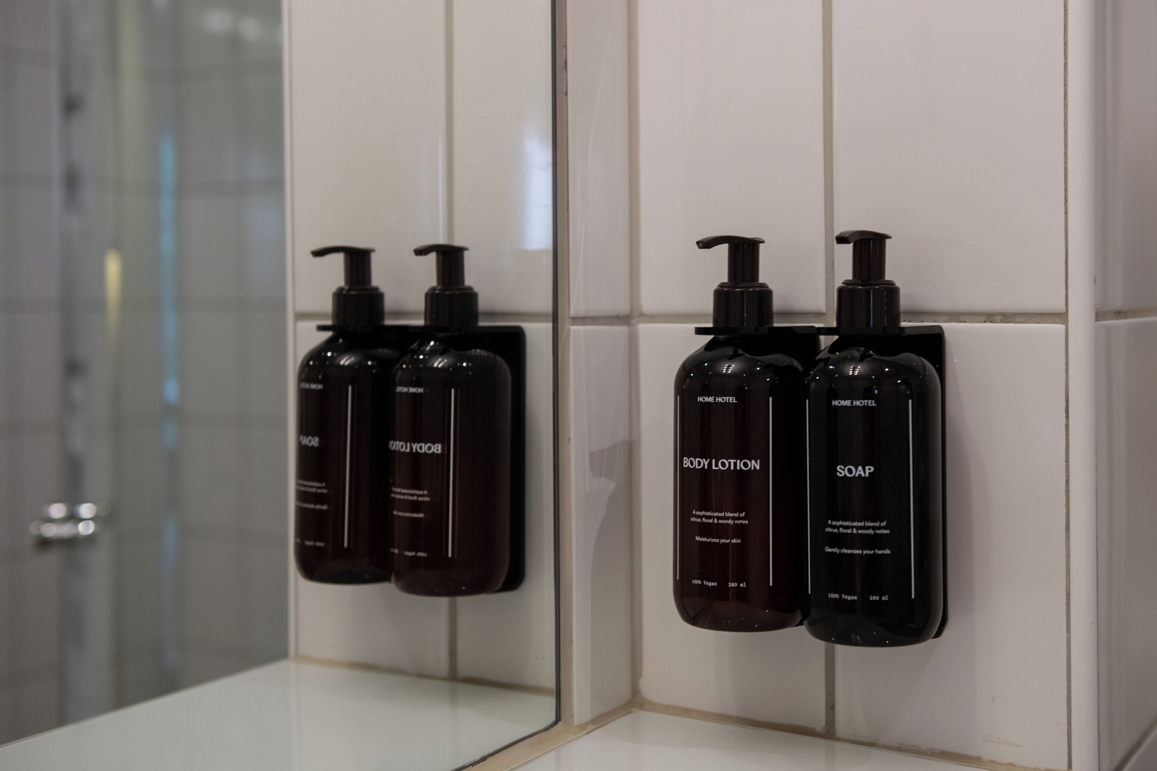 Ett badrum med en spegel som reflekterar tre flaskor med hygienprodukter: kroppslotion, tvål och duschgel.