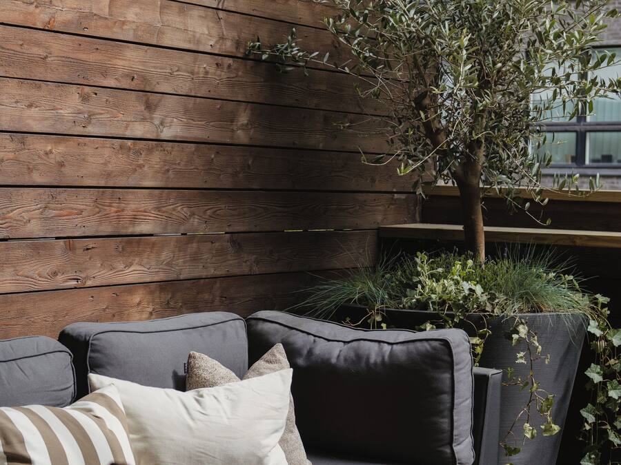 A modern outdoor seating area with a wooden wall, a grey sofa, and a small table.