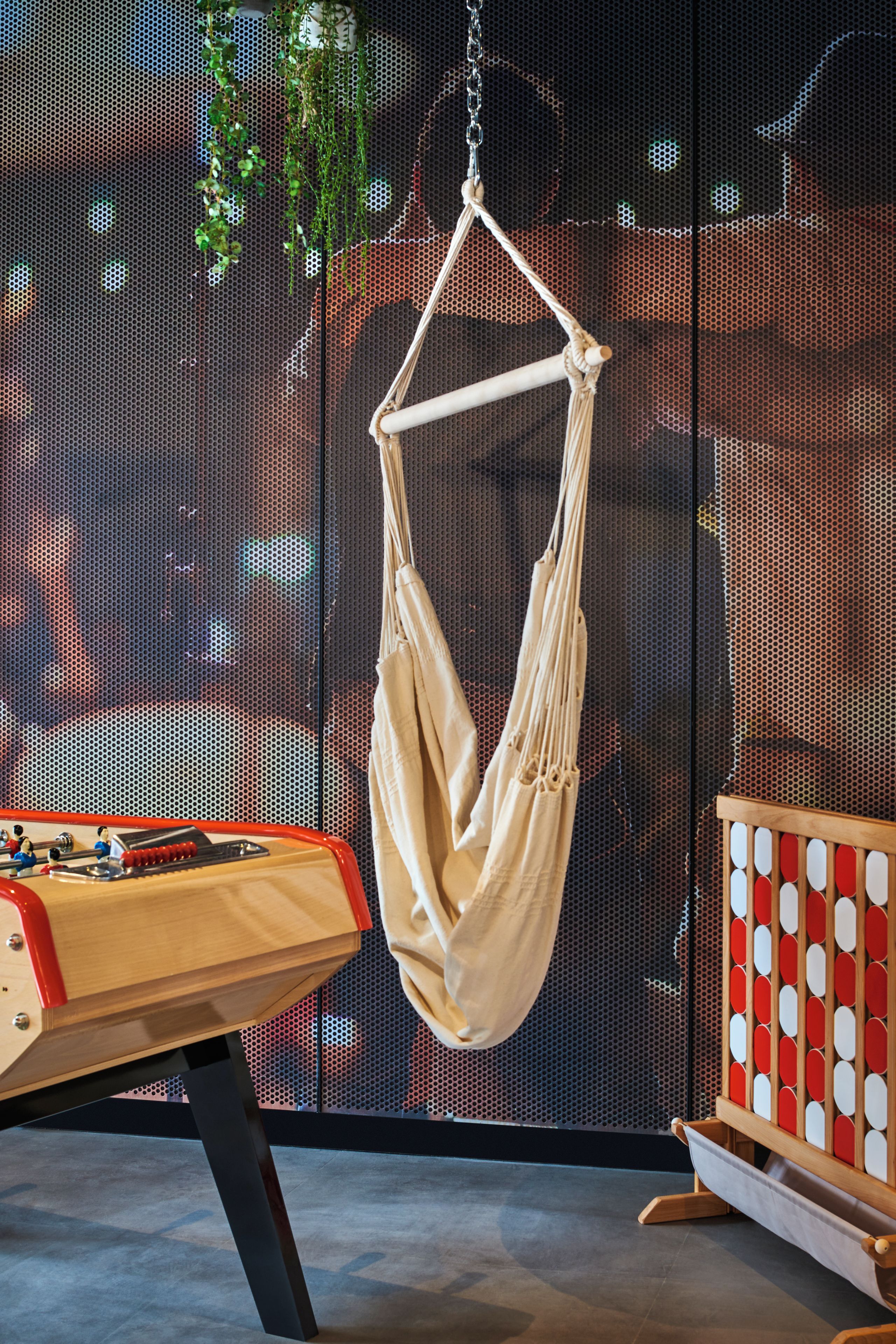 A room with a hanging chair, a foosball table, and a wall with a perforated design.