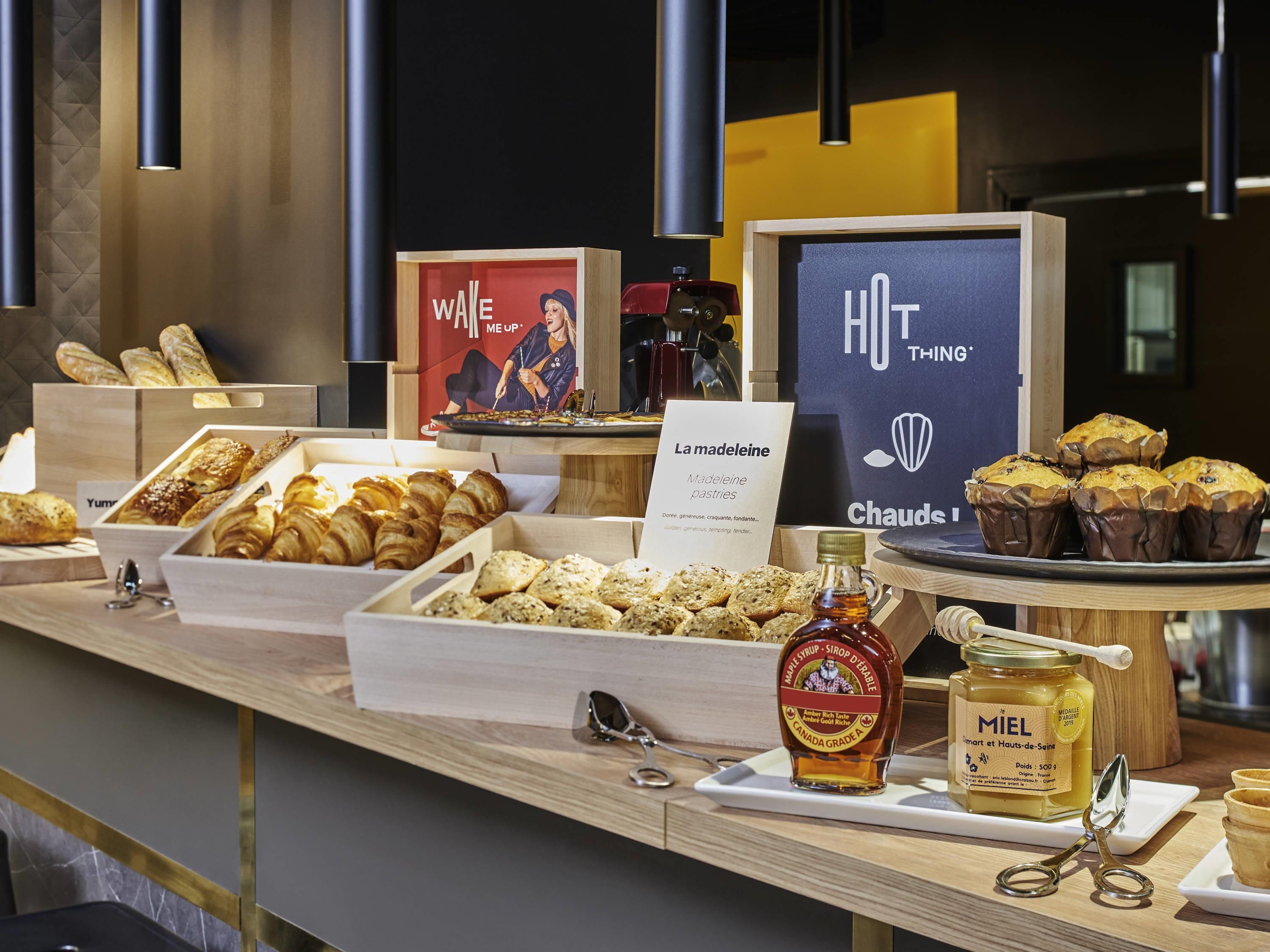 Buffet com diversos pastéis, placa indicando pastéis 'La Madeleine' e um pote de mel 'MIEL'.