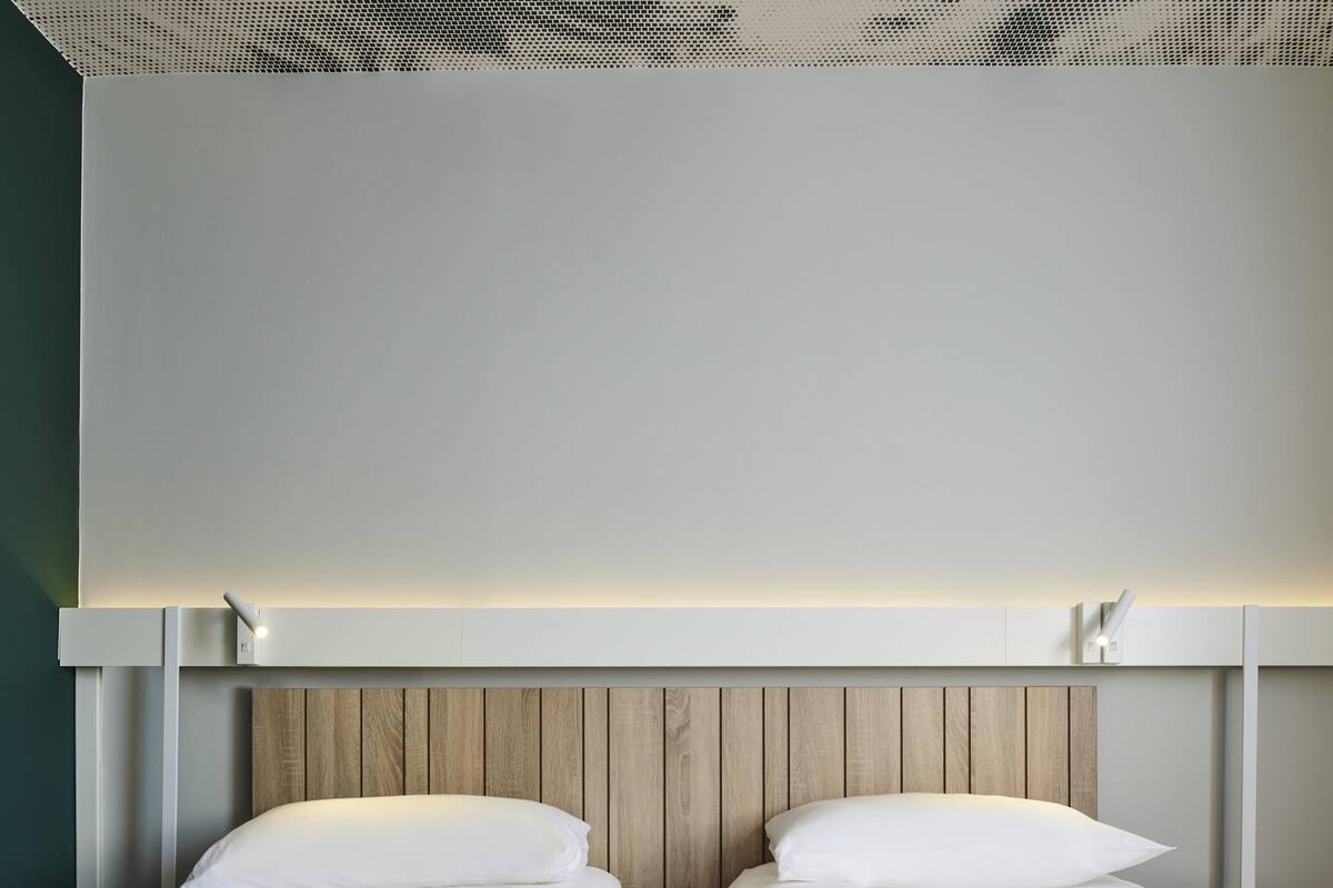 A modern hotel room with two beds, wooden headboard, and a ceiling with a perforated design.