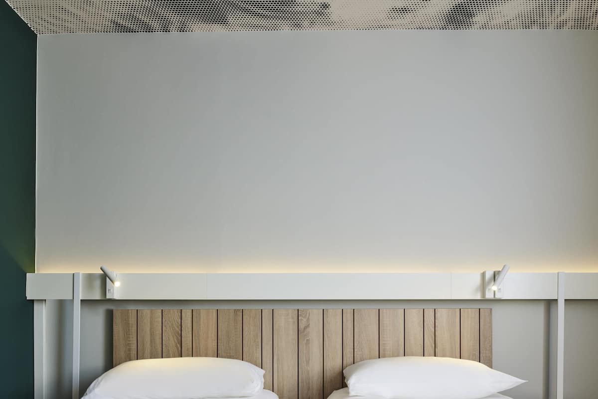 A hotel room with two beds, a wooden headboard, and a ceiling with a perforated design.