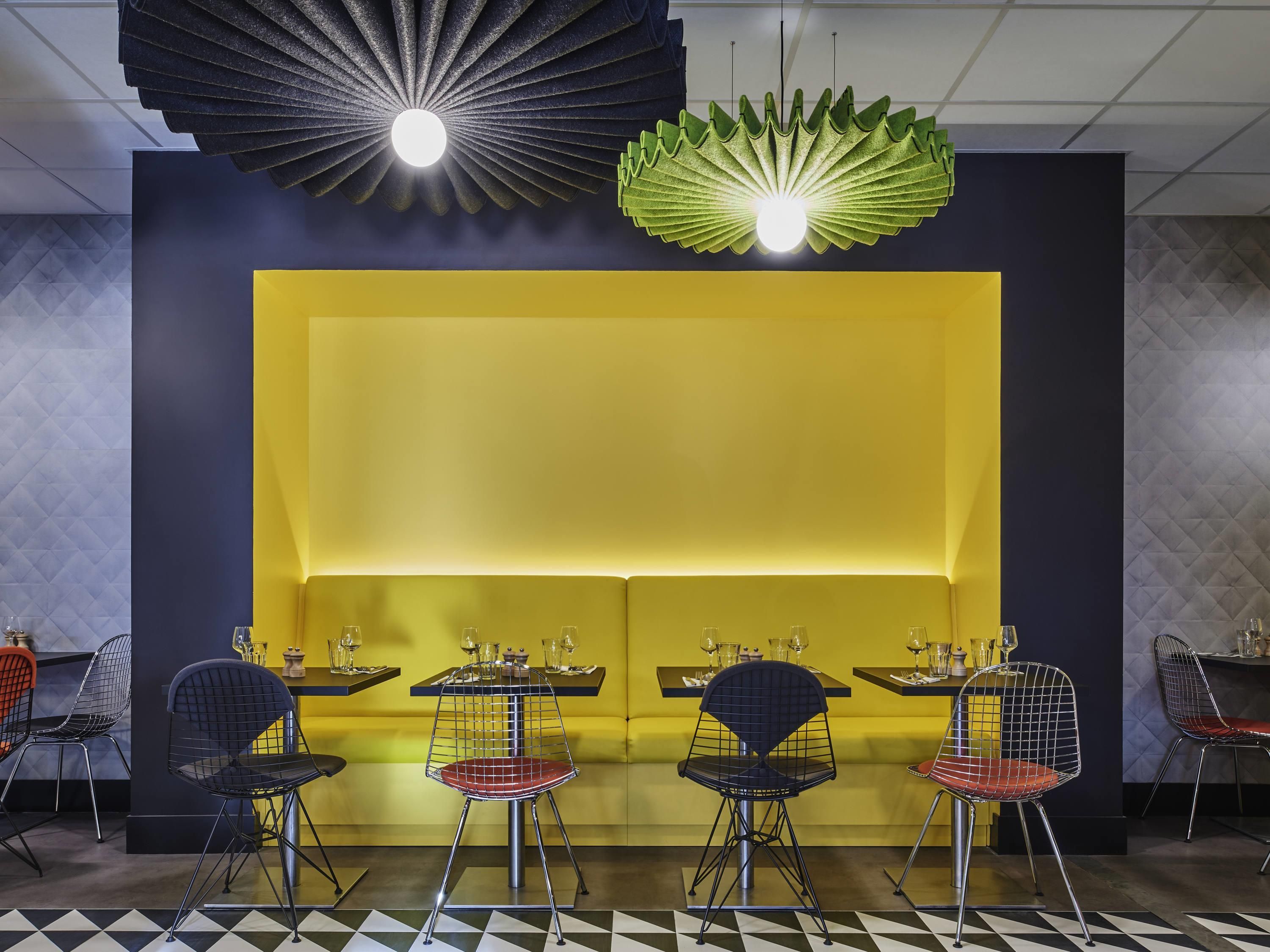 Ein Restaurant mit gelber Akzentwand, schwarz-weiß kariertem Boden und Stuhlgestellen aus Draht.