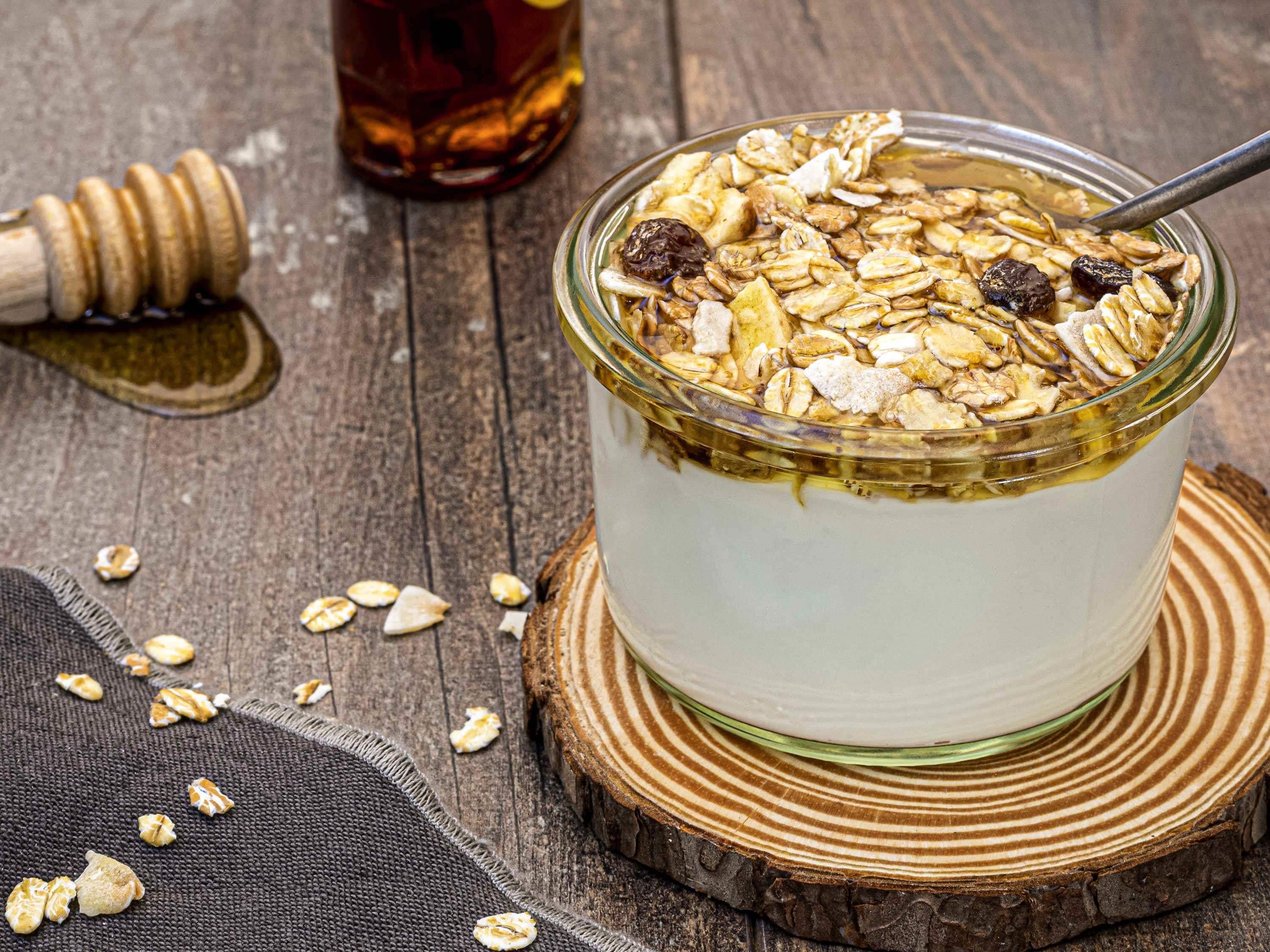 A glass bowl of yogurt topped with granola and raisins, placed on a wooden coaster.