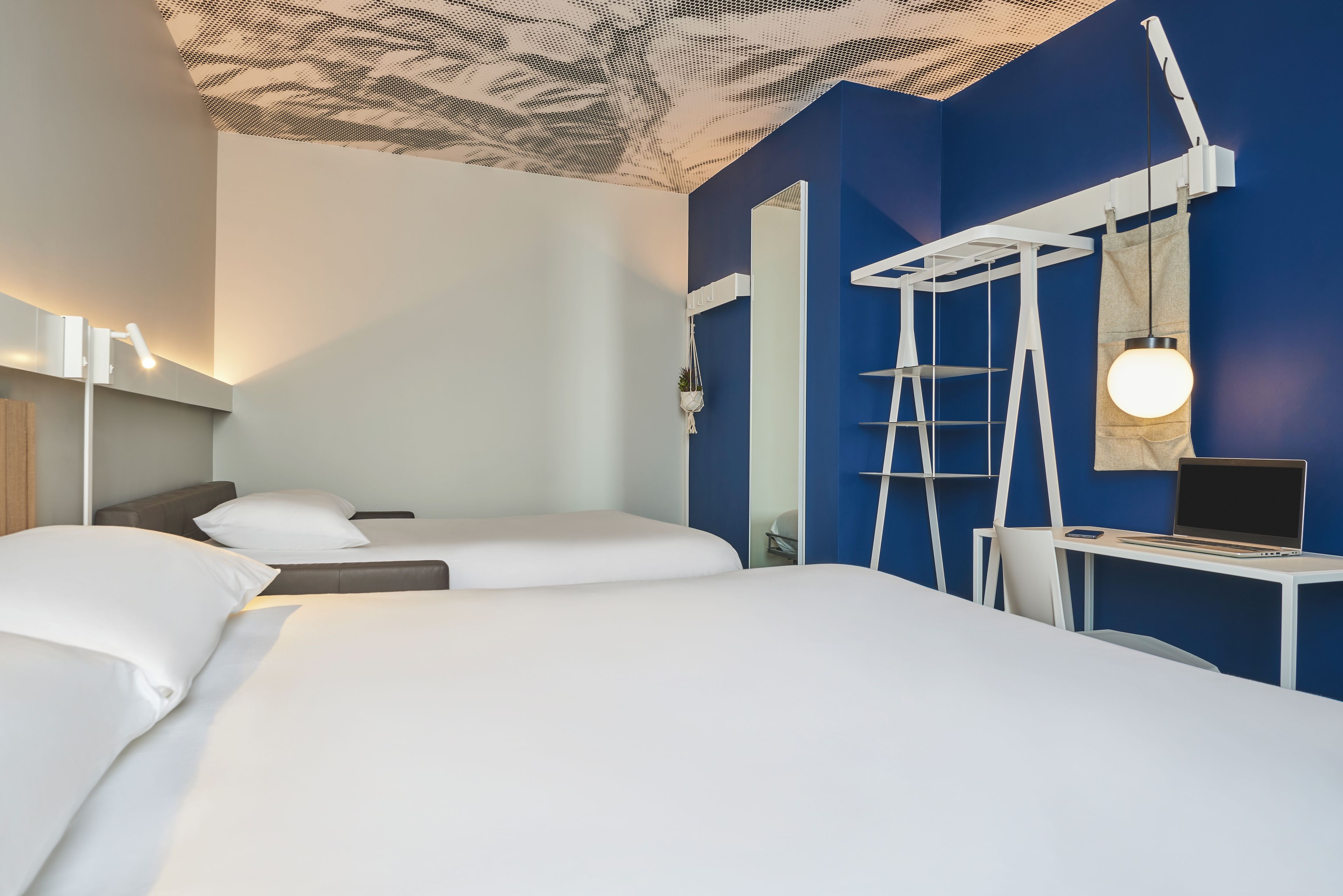 Una camera d'albergo con un letto, una scrivania con un portatile, una sedia e uno specchio.