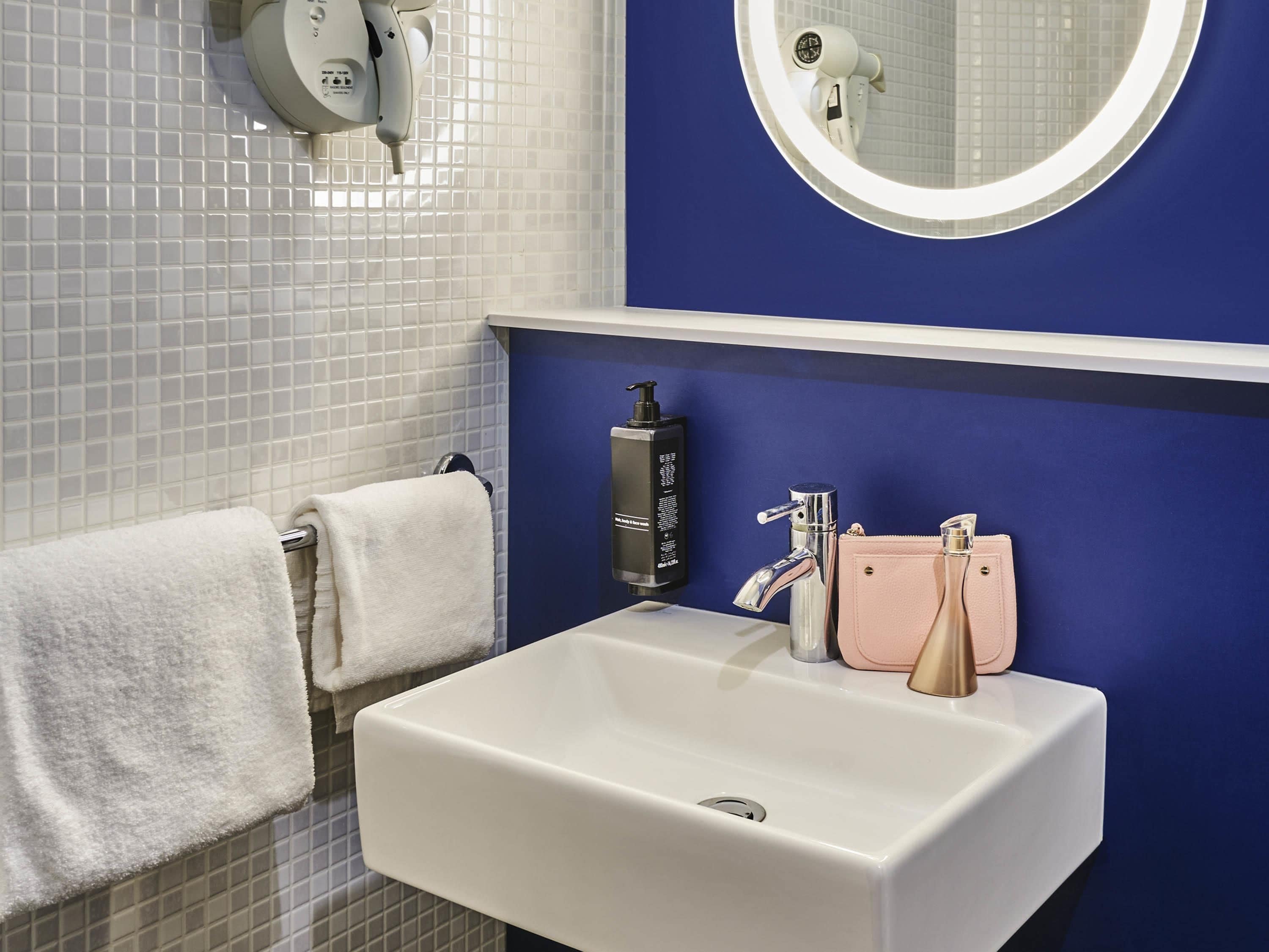 Un baño con un lavamanos blanco, un espejo, un perchero para toallas y una pared azul.