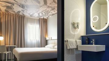 A hotel room with a bed, a desk, and a bathroom with a mirror and sink.