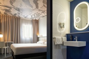 Een hotelkamer met een bed, een bureau en een badkamer met een spiegel en wastafel.