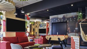 A modern living room with a red sofa, a foosball table, and a TV. - ibis Clamart Paris Velizy (Clamart)