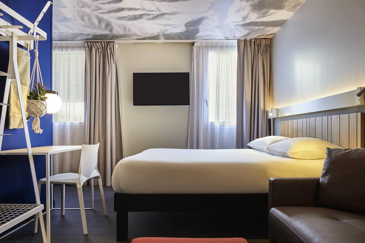 A hotel room with a bed, a desk, a chair, a couch, and a TV.