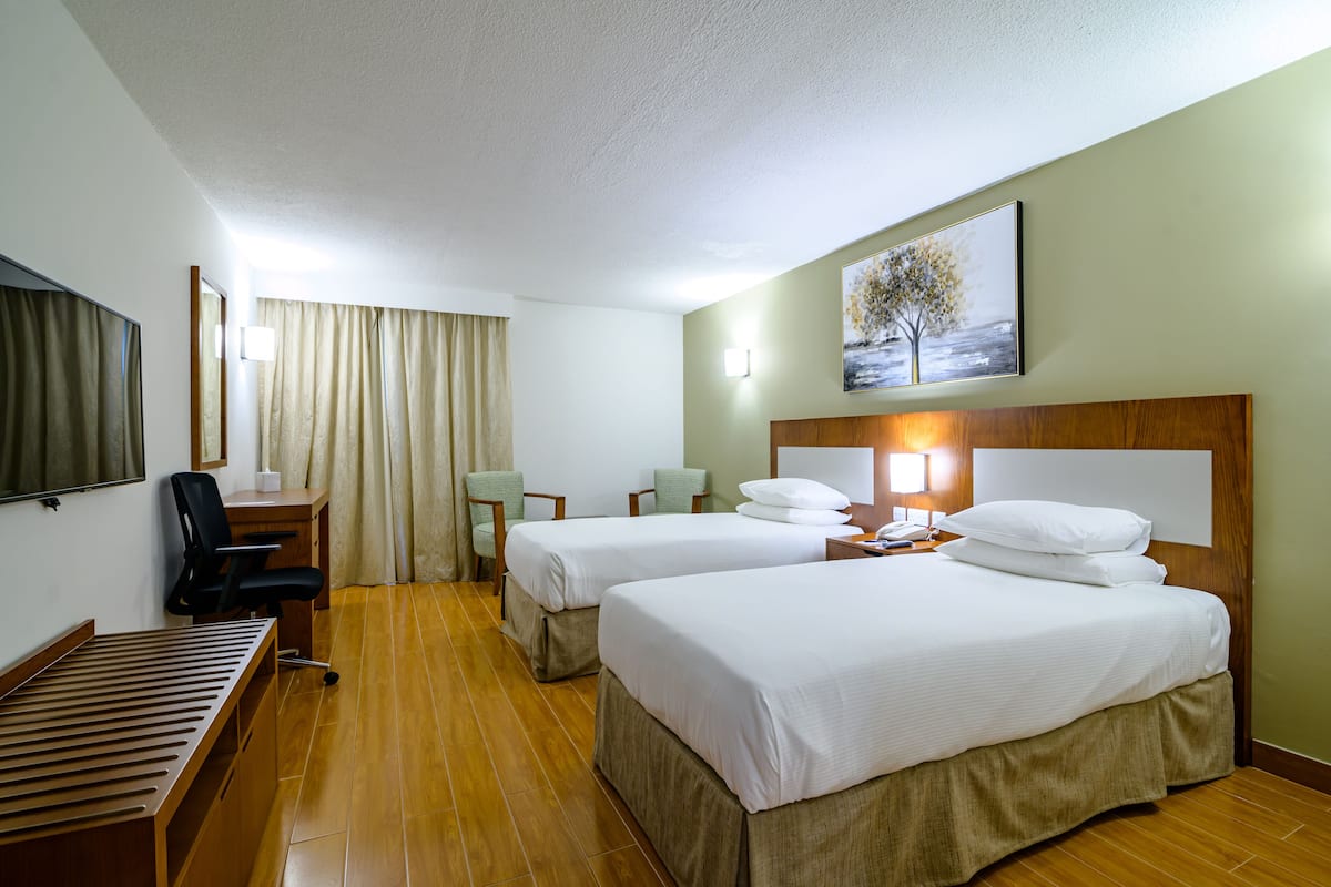 Une chambre d’hôtel avec deux lits, un bureau, une chaise, une télévision et un tableau au mur.