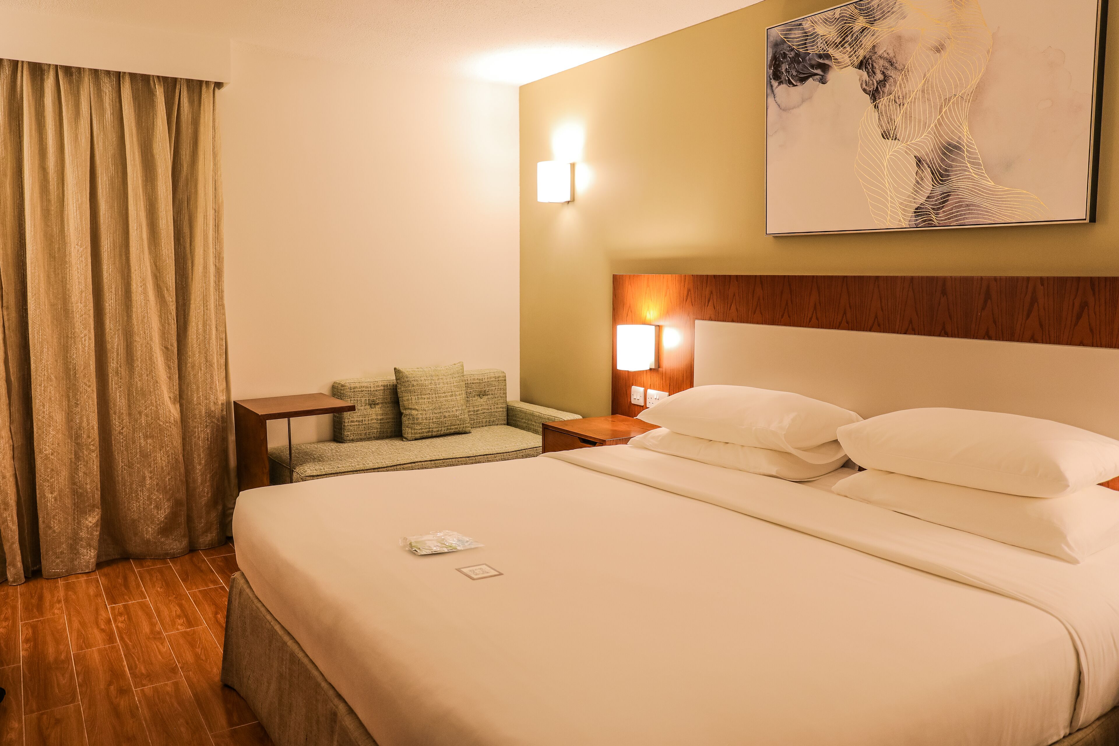Une chambre d’hôtel avec un grand lit, une table de chevet, une lampe, un tableau au mur et une fenêtre avec des rideaux.