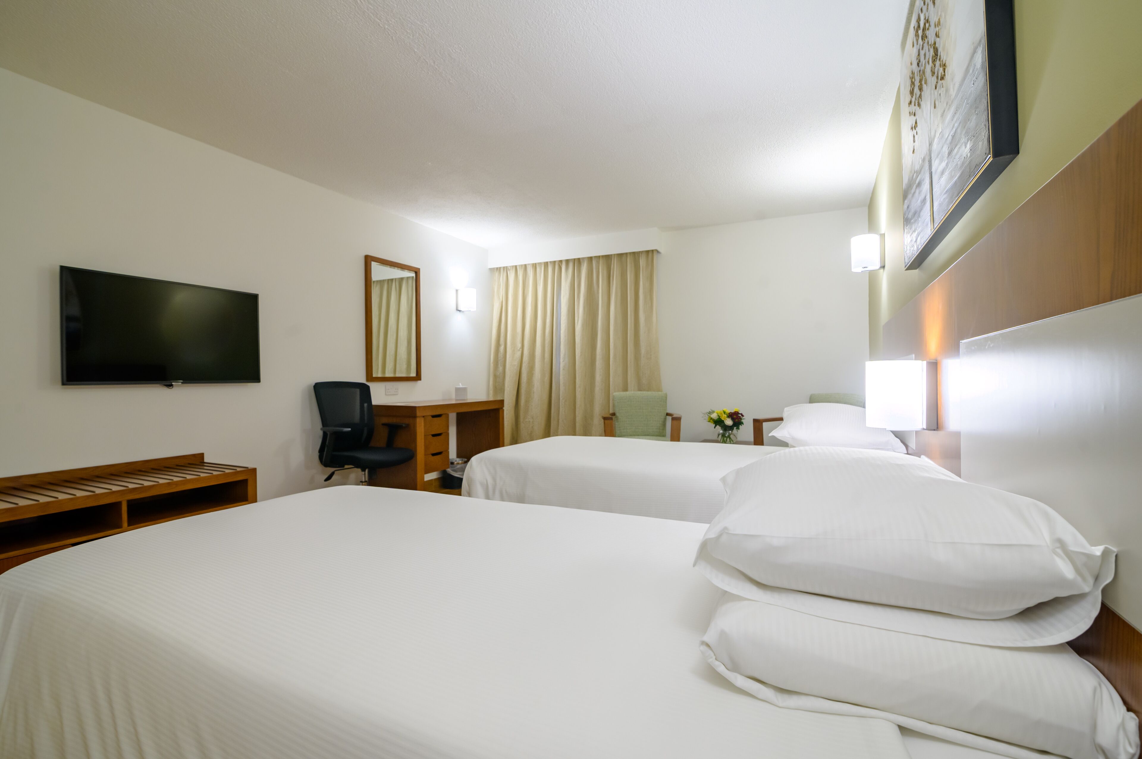 A hotel room with two beds, a desk, a chair, a TV, and a painting on the wall.