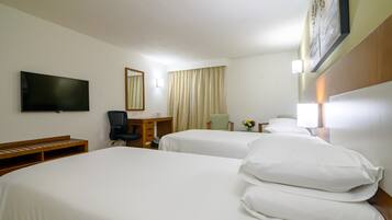 A hotel room with two beds, a desk, a chair, a TV, and a painting on the wall.