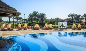 Área de piscina com espreguiçadeiras e uma cama com dossel.