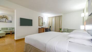 Habitación de hotel con una cama grande, un escritorio, una silla, un sofá y un televisor en la pared.