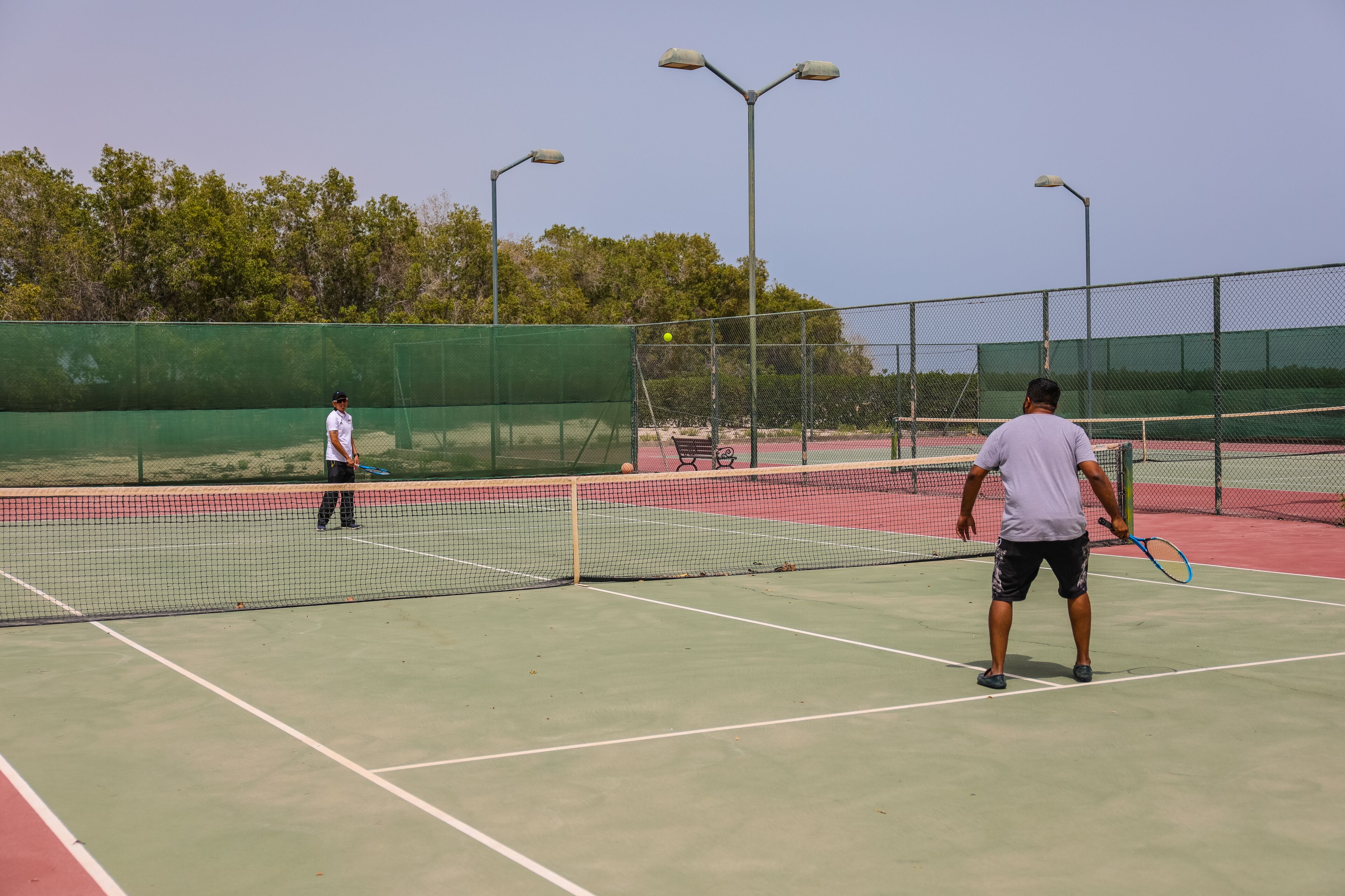 Un court de tennis avec deux joueurs, un filet et une clôture qui l’entoure.