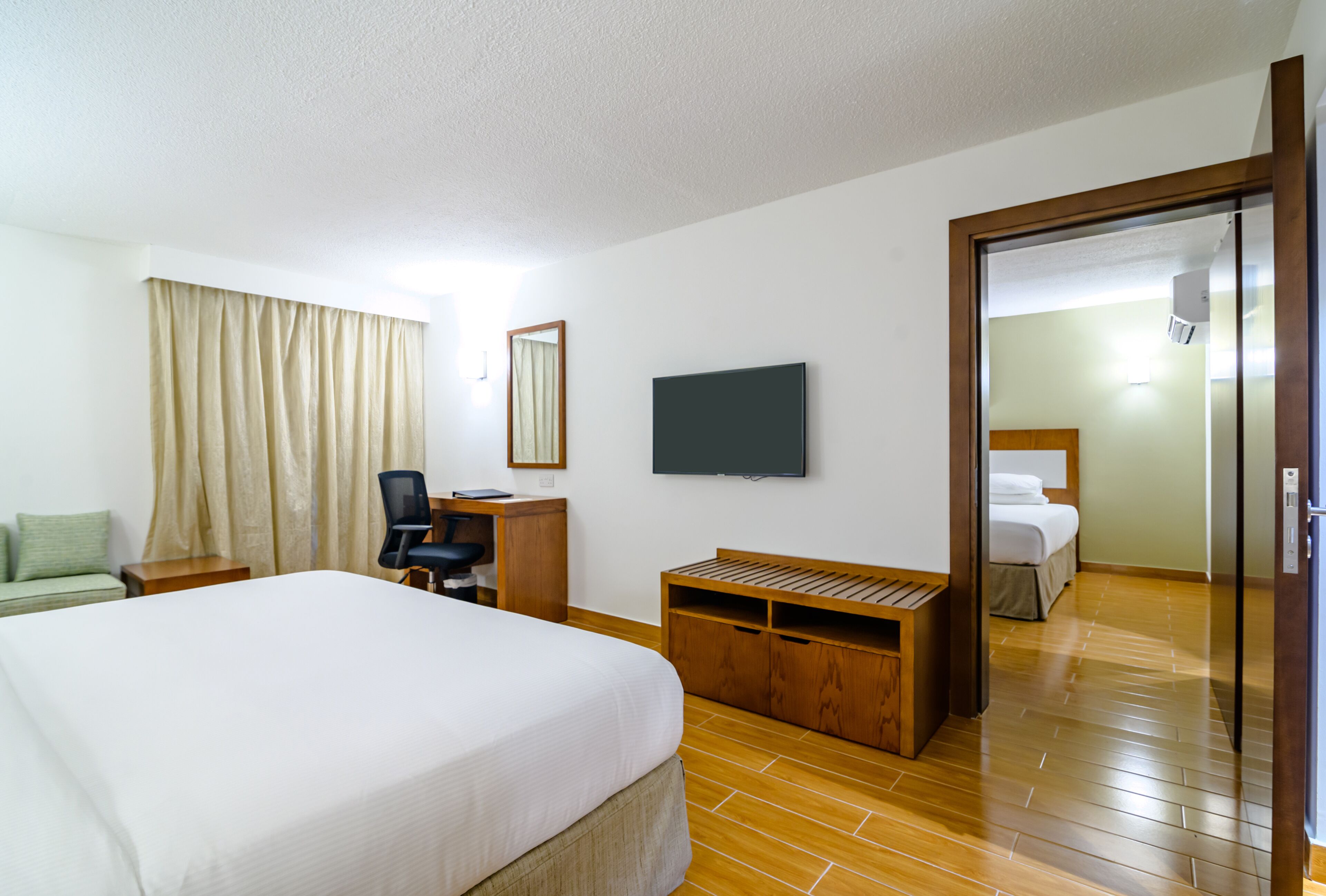 Ein Hotelzimmer mit einem großen Bett, einem Schreibtisch mit Stuhl, einem an der Wand befestigten Fernseher und einer Holzbank.