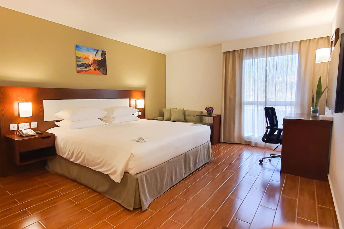 Une chambre d’hôtel avec un grand lit, des lampes de chevet, un bureau, une chaise et un tableau au mur.