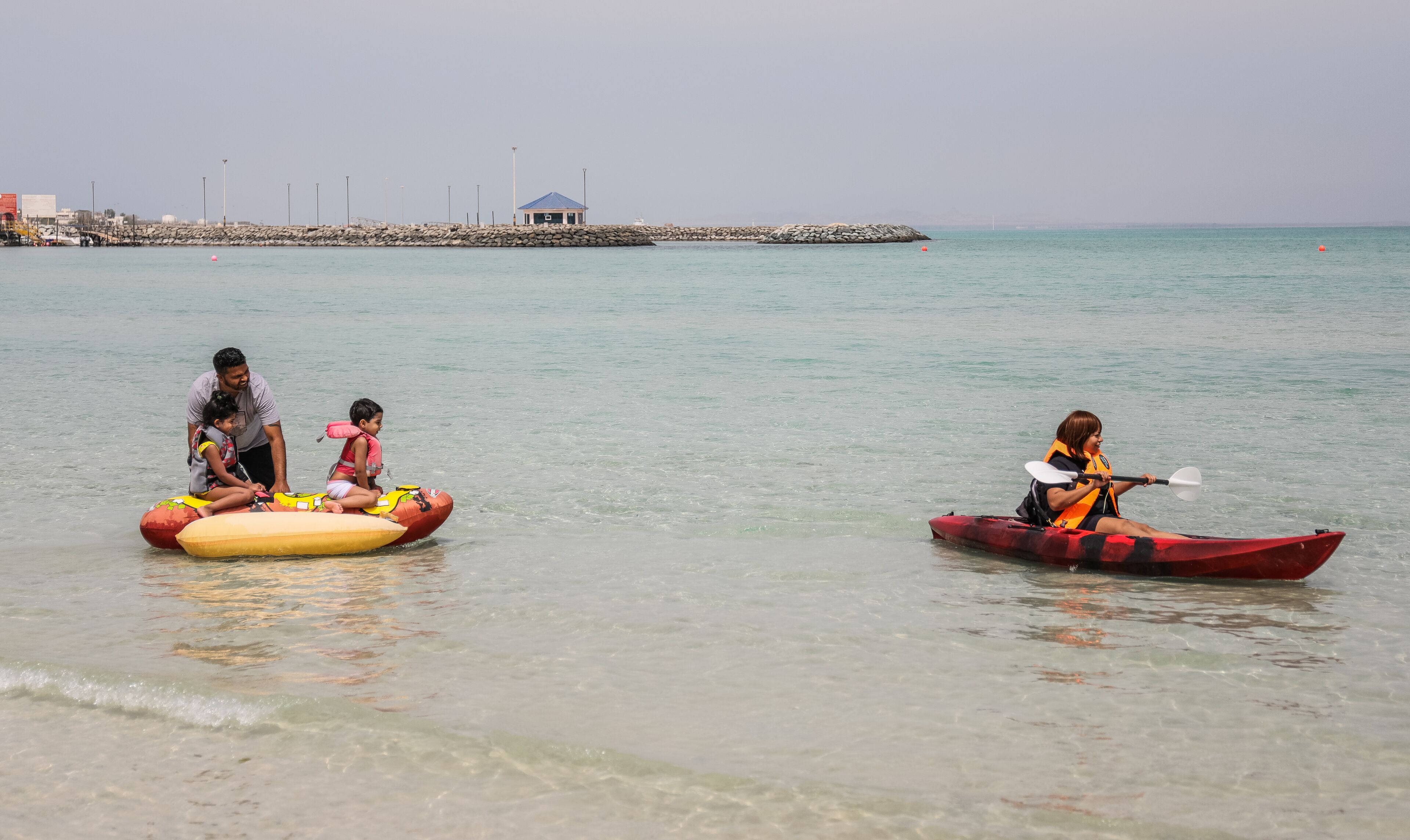 A calm beach scene with people in inflatable boats and a kayak.