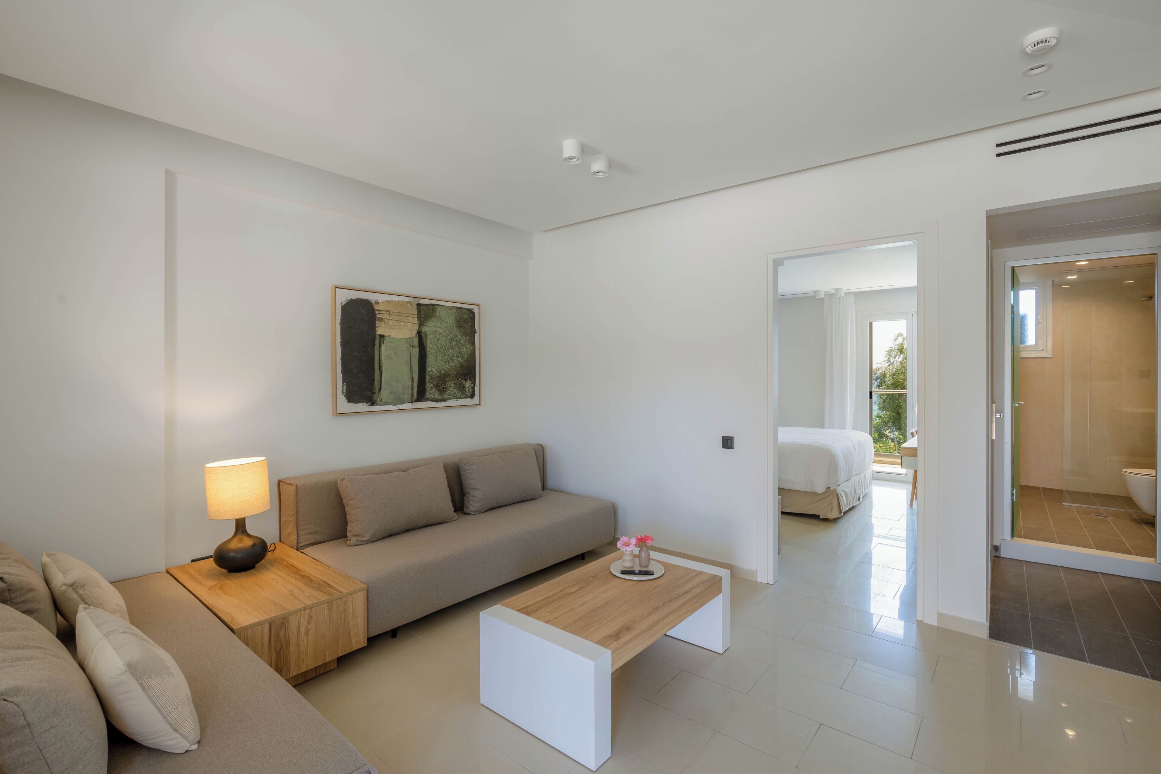 Un salon moderne avec un canapé, une table basse et une lampe. Un tableau orne le mur, et on peut apercevoir une salle de bain à travers une porte ouverte.