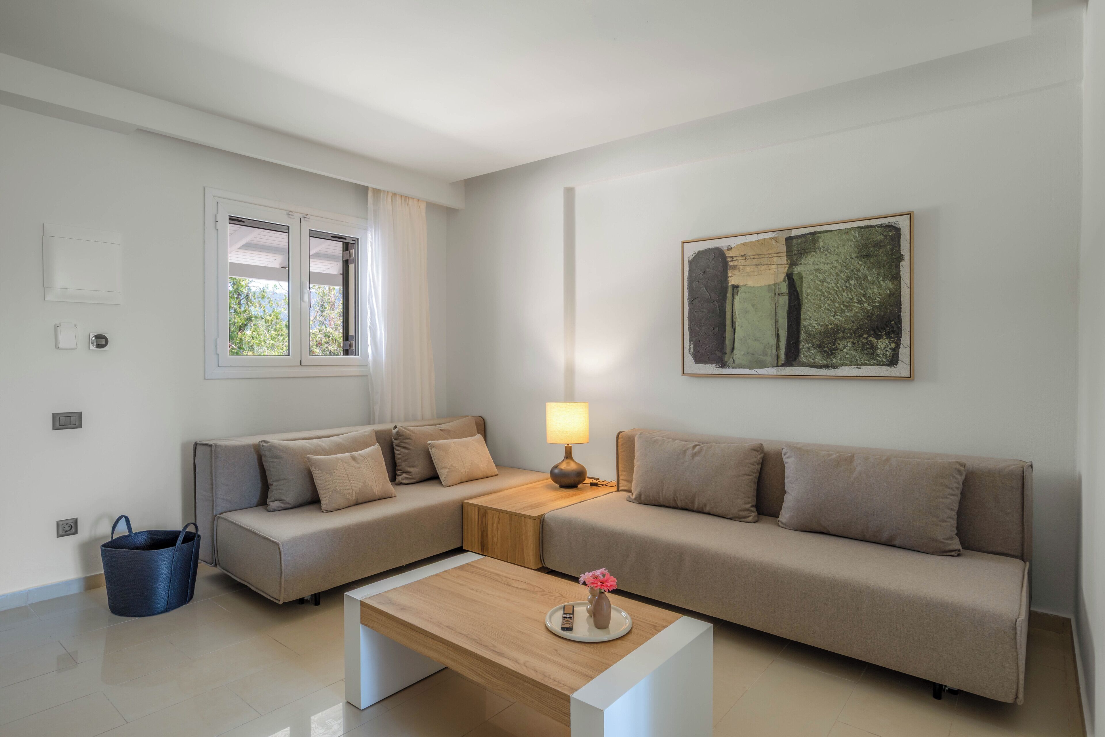 Una sala de estar moderna con dos sofás, una mesa de centro, una lámpara, un cuadro y una ventana con cortinas.