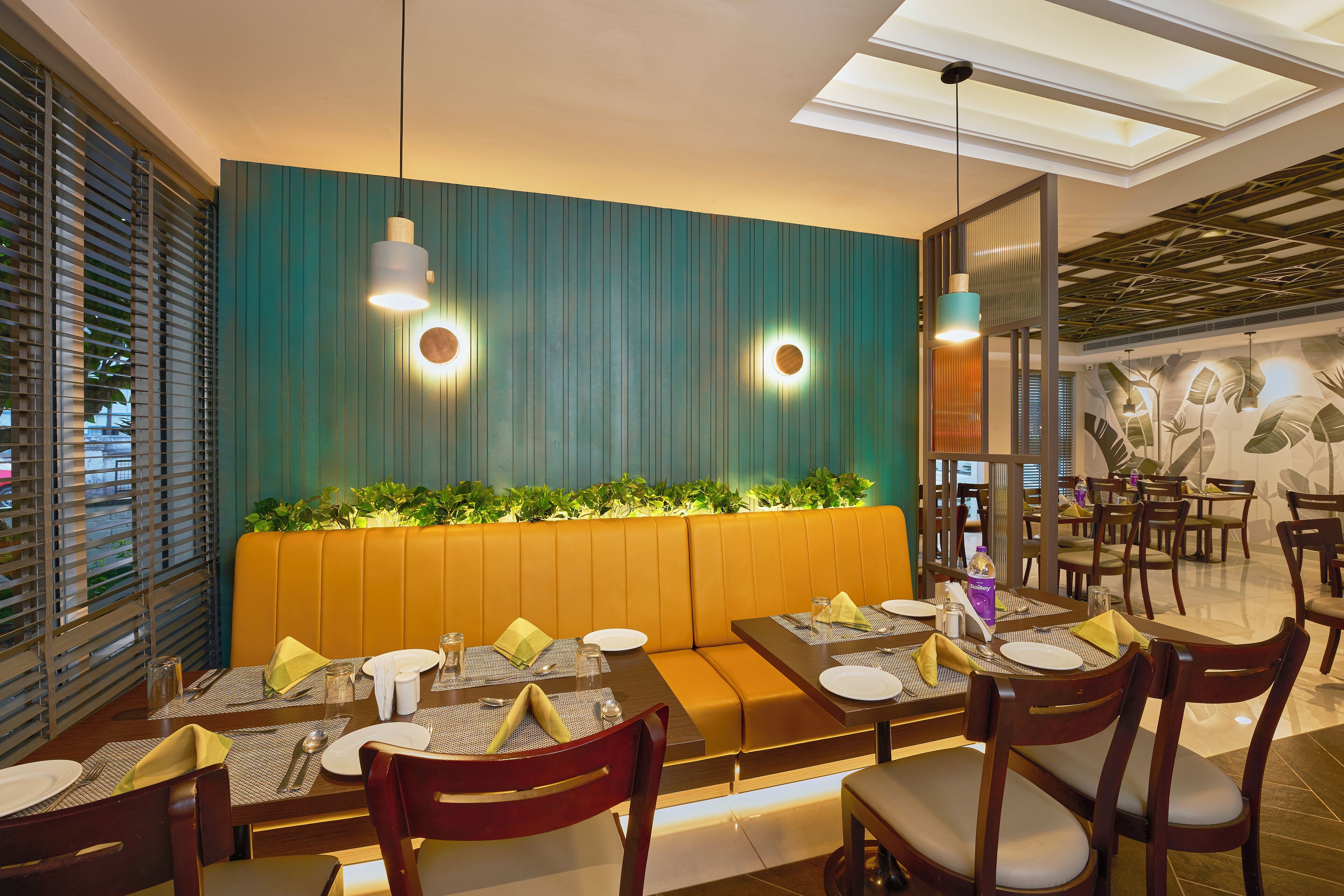 A restaurant with a teal-colored wall, wooden tables, and a cushioned bench.