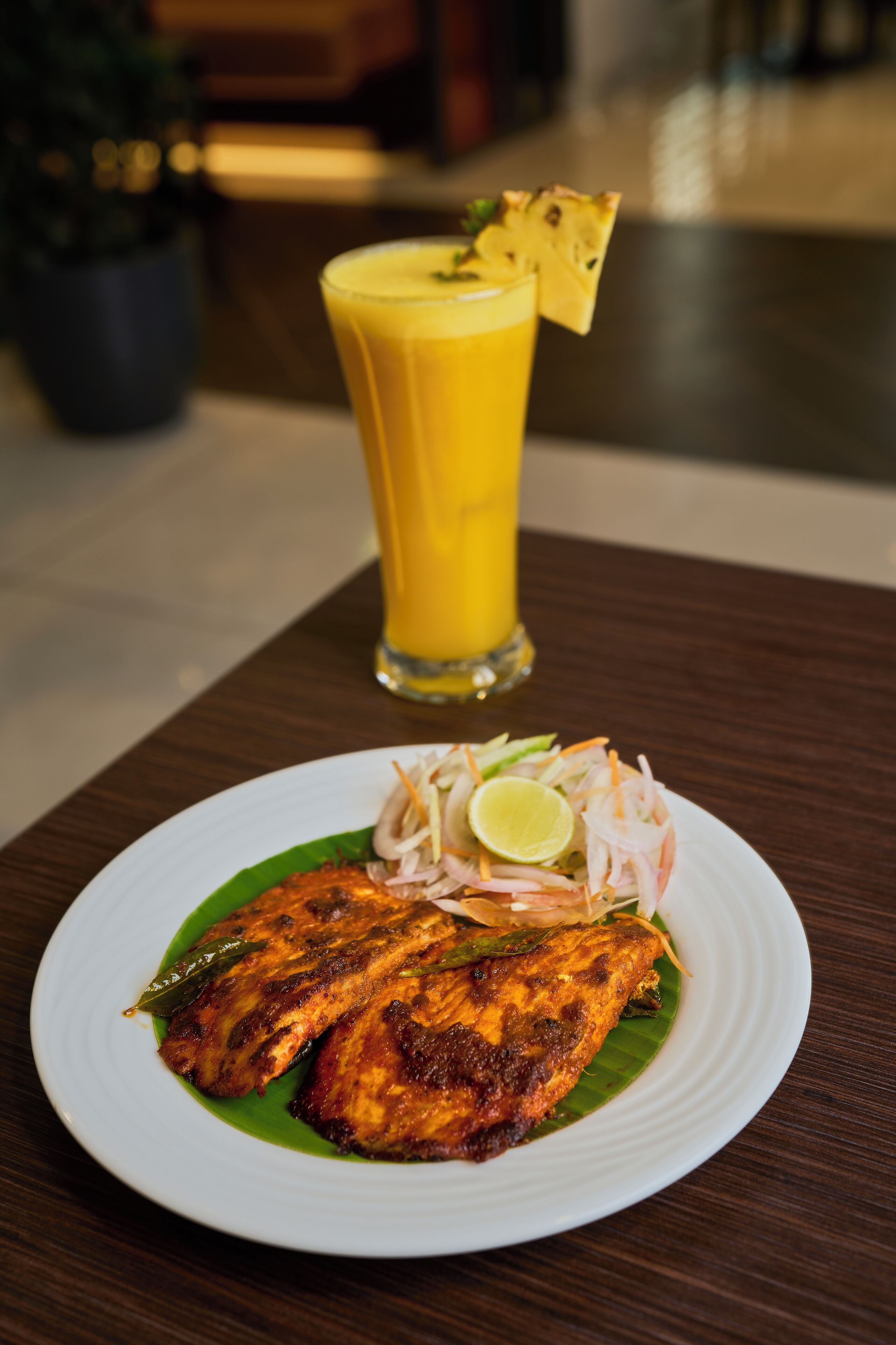 A plate of grilled fish with a side salad and a glass of orange juice on a wooden table.