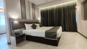 Habitación de hotel moderna con una cama grande, una mesita de noche con teléfono y un cabecero con iluminación integrada, y un fondo de cortina oscura.