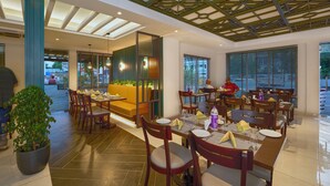 Un restaurante con mesas y sillas de madera, una planta grande en maceta y un techo con diseño geométrico.