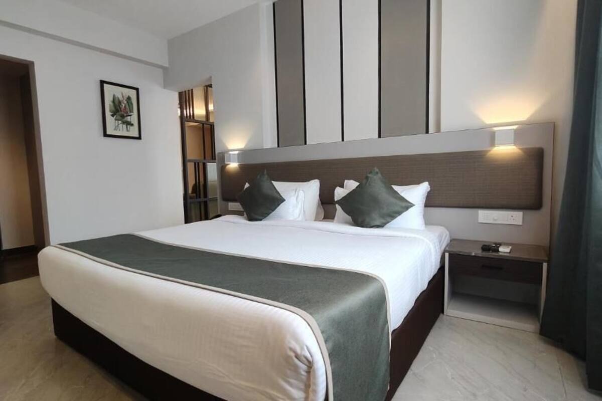 A modern hotel room with a large bed, a nightstand, a wall-mounted light, and a door.