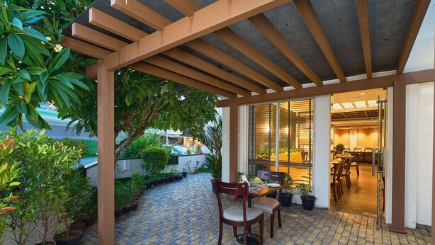 Un área de estar al aire libre cubierta con plantas en macetas, una pérgola de madera y vista hacia el espacio interior comedor.