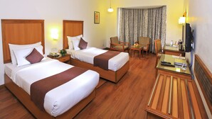 Quarto de hotel com duas camas, uma escrivaninha, uma cadeira, uma televisão e uma janela com cortinas.
