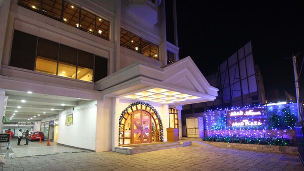 Entrada de hotel com uma grande porta em arco, área coberta e área ajardinada com plantas iluminadas.