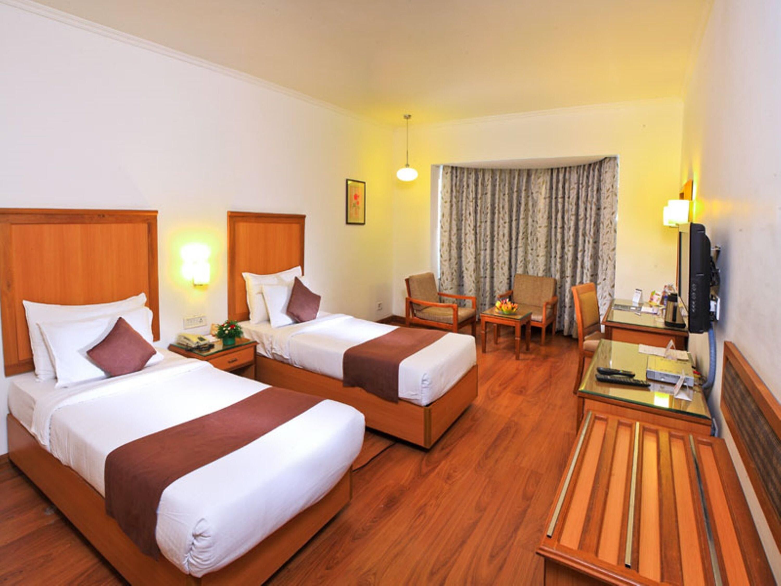 A hotel room with two beds, a desk, a chair, a television, and a window with curtains.