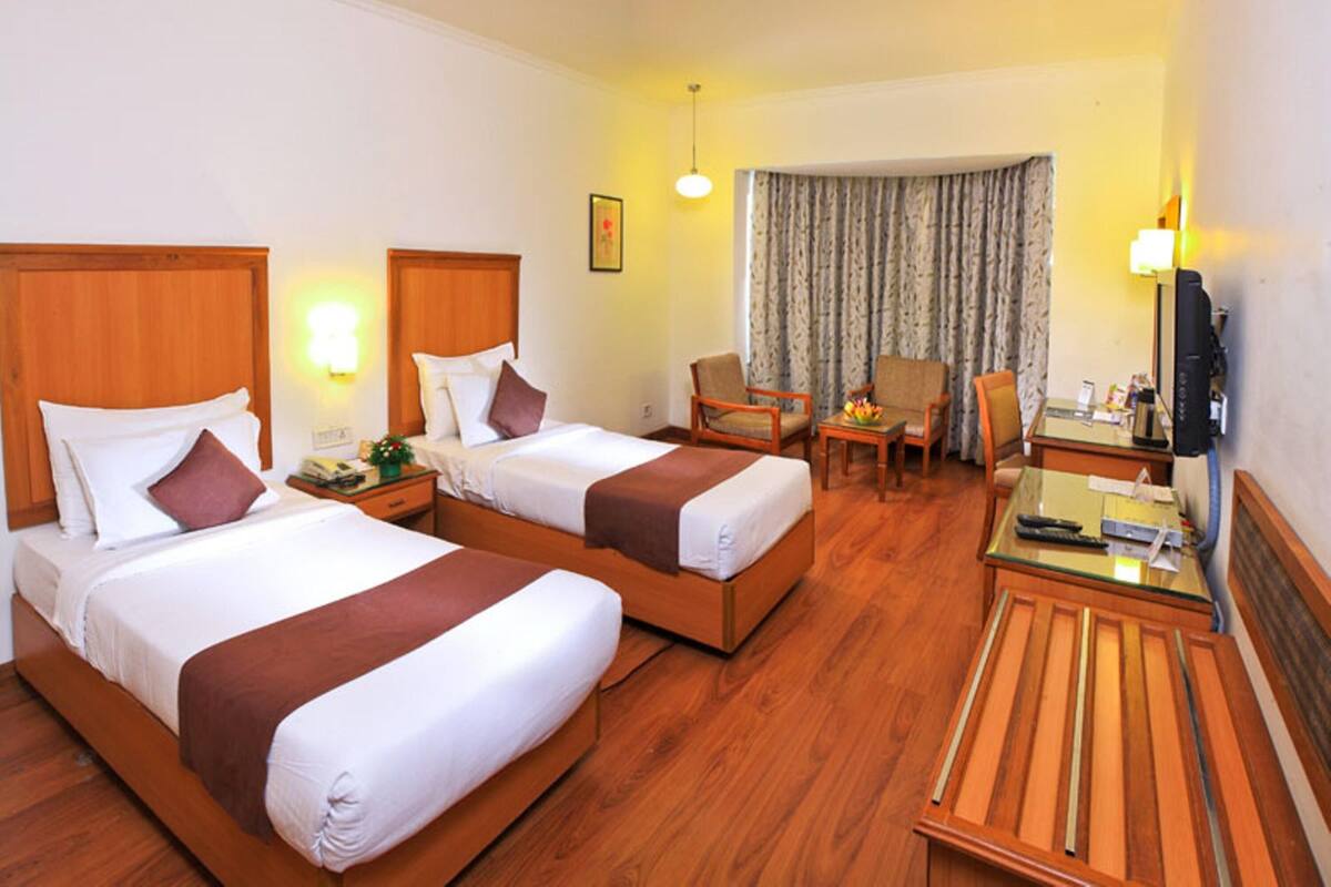 A hotel room with two beds, a desk, a chair, a television, and a window with curtains.
