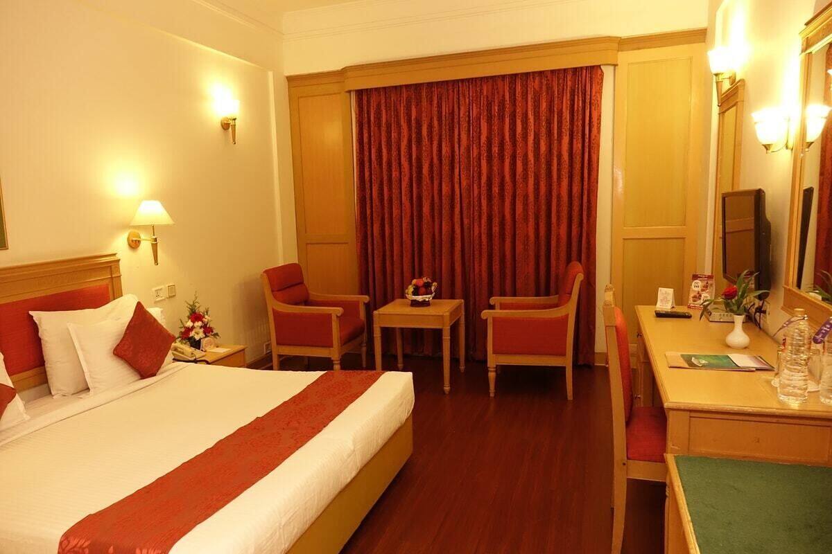A hotel room with a bed, two chairs, a desk, a lamp, a mirror, and a curtain.