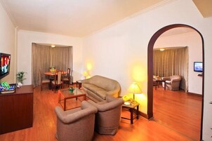 A hotel room with a sofa, two armchairs, a coffee table, a TV, and a desk with a computer.