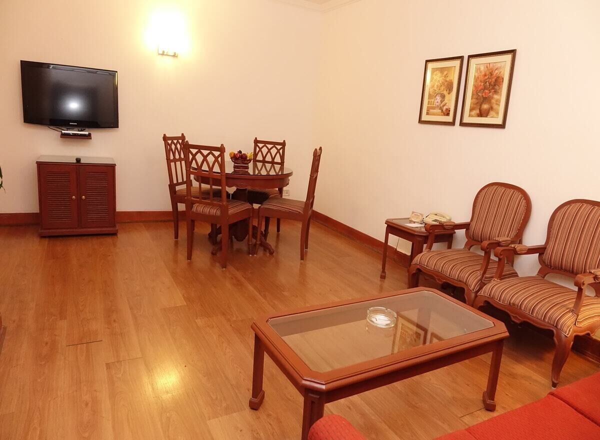 Un salon avec un plancher en bois, une table basse en verre, un téléviseur, une table à manger avec des chaises et deux tableaux encadrés accrochés au mur.