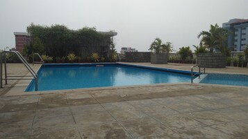 Una piscina rectangular con un borde de baldosas, rodeada de plantas en macetas y un muro de piedra.