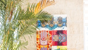 A room with a wooden sofa, colorful cushions, a wall tapestry, and a potted plant. - Liwan Hotel (Amman)