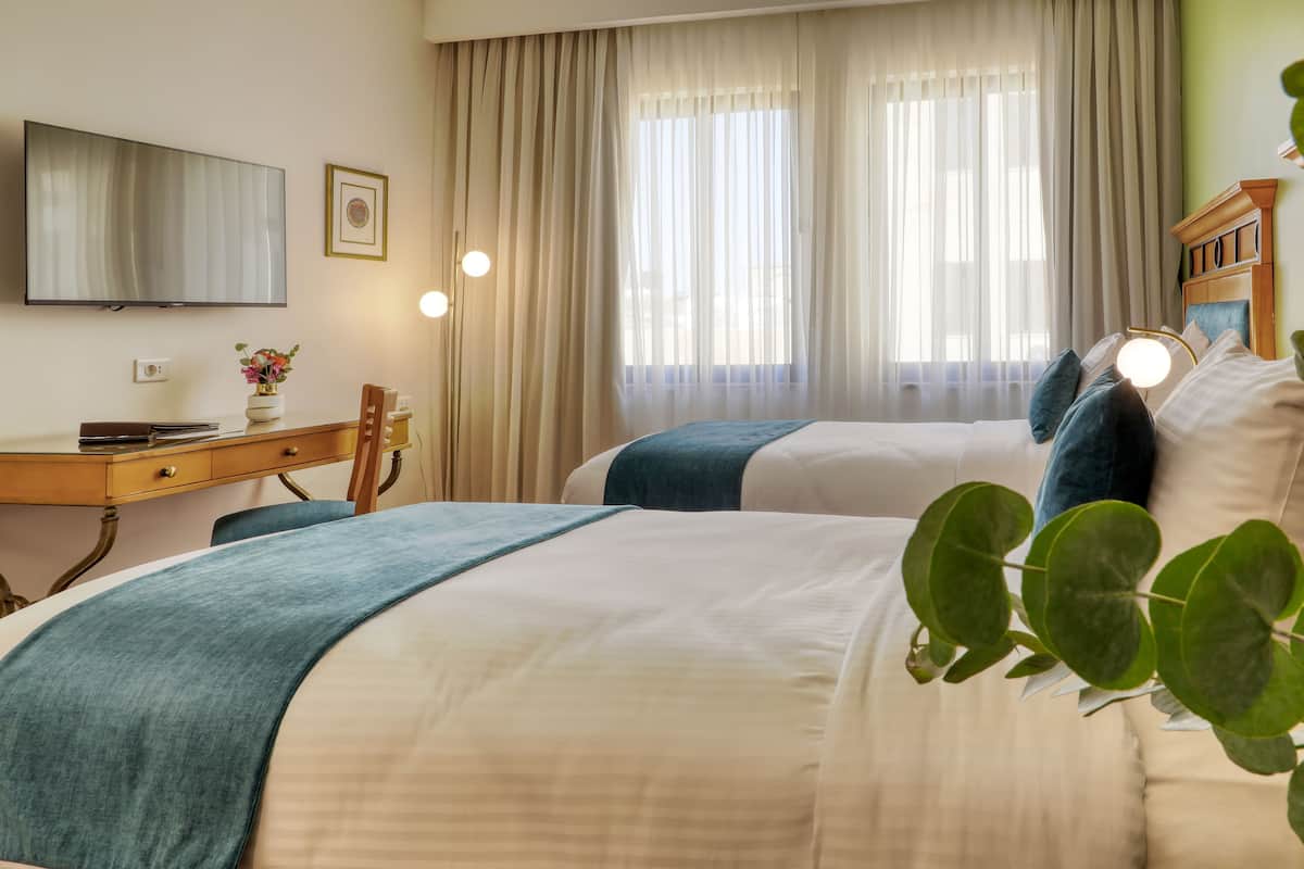 A hotel room with two beds, a desk, a television, and a window with curtains.