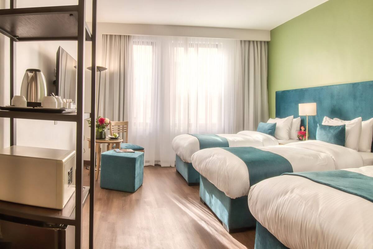 A hotel room with two beds, a desk, a chair, and a small table with a vase of flowers.